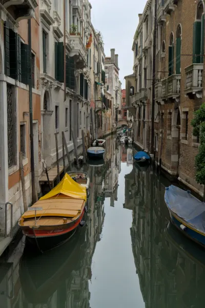 Uzak kanal u Veneciji sa čamcima i reflektujućim zgradama, savršen za zidnu umetnost.