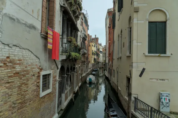 Uzak venecijanski kanal sa šarenim zgradama, vešom koji visi sa balkona i čamcima u vodi.