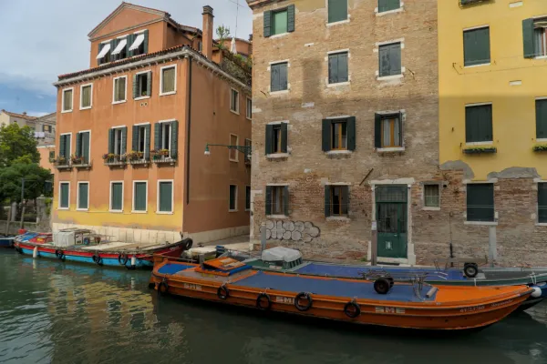 Blick auf venezianische Kanäle mit Booten vor historischen orangefarbenen und gelben Gebäuden mit grünen Fensterläden.