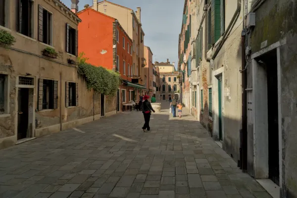 Fine art fotografija uske ulice u Veneciji sa zgradama pastelnih boja i popločanim tlom.
