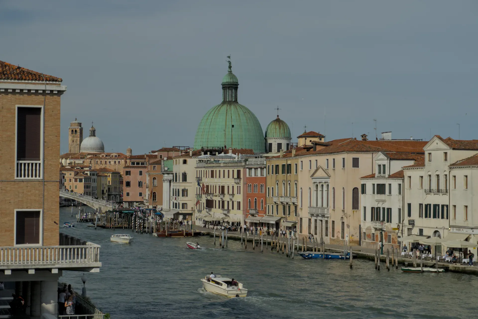 Landscape shot of the Grand Canal in Venice, Italy, with traditional buildings and a prominent green dome in the background.
