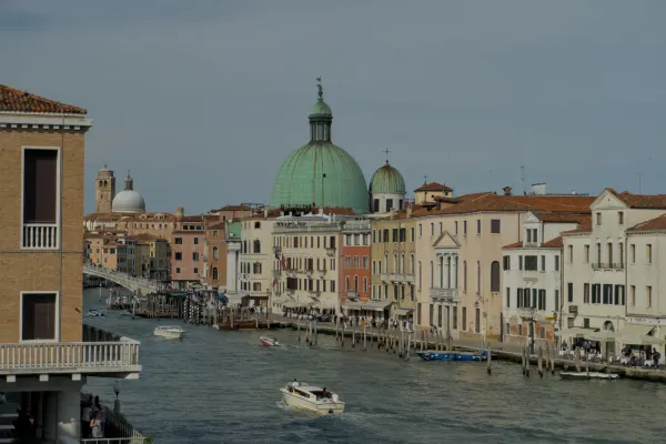 Landschaftsaufnahme des Canal Grande in Venedig, Italien, mit traditionellen Gebäuden und einer prominenten grünen Kuppel im Hintergrund.