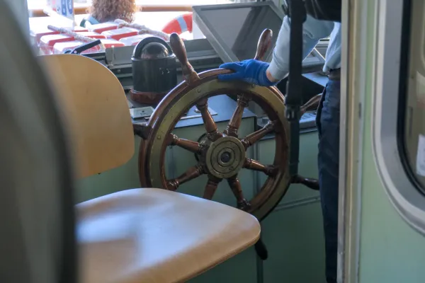 Ein hölzernes Steuerrad eines Vaporetto in Venedig, gehalten von einer Person mit blauen Handschuhen.