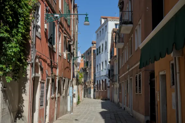 Eine sonnige, Kopfsteinpflaster-Gasse in Venedig, gesäumt von traditionellen italienischen Häusern mit warmen Fassadenfarben.