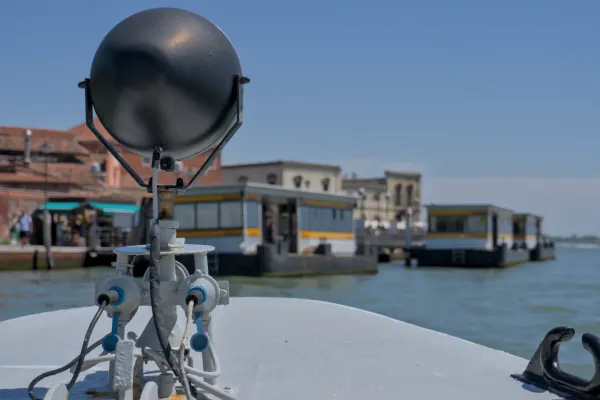 Ein Wasserbus nähert sich der Insel Murano, mit Gebäuden und dem Wasser im Hintergrund.