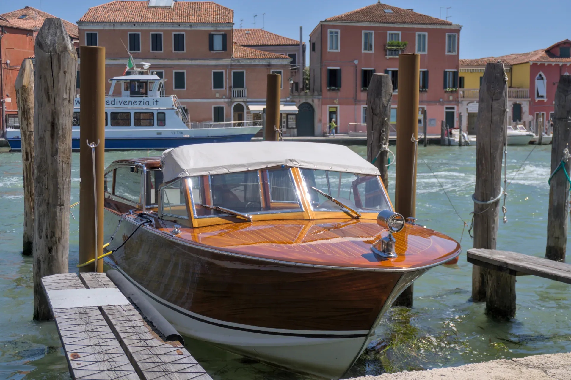 Wooden motorboat anchored at the dock on the island of Murano in Venice, with traditional buildings in the background.
