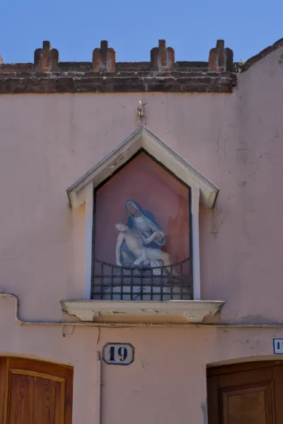 Photographie d'art d'une représentation de la Pietà sur l'île de Murano, Italie, avec un bâtiment rose enduit et un ciel bleu.