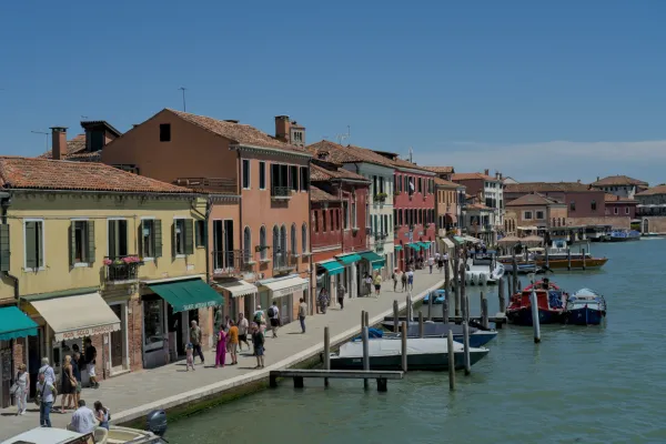 Šarene kuće duž kanala na ostrvu Murano, Venecija, sa čamcima i ljudima, tokom sunčanog dana.