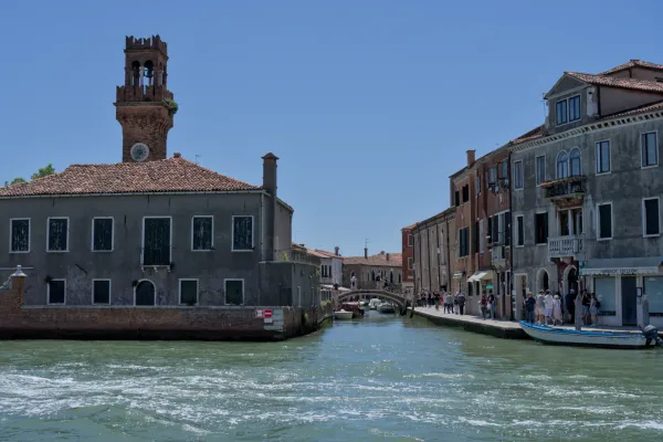 Kanal na ostrvu Murano u Veneciji sa starim tornjem od cigle i istorijskim zgradama.