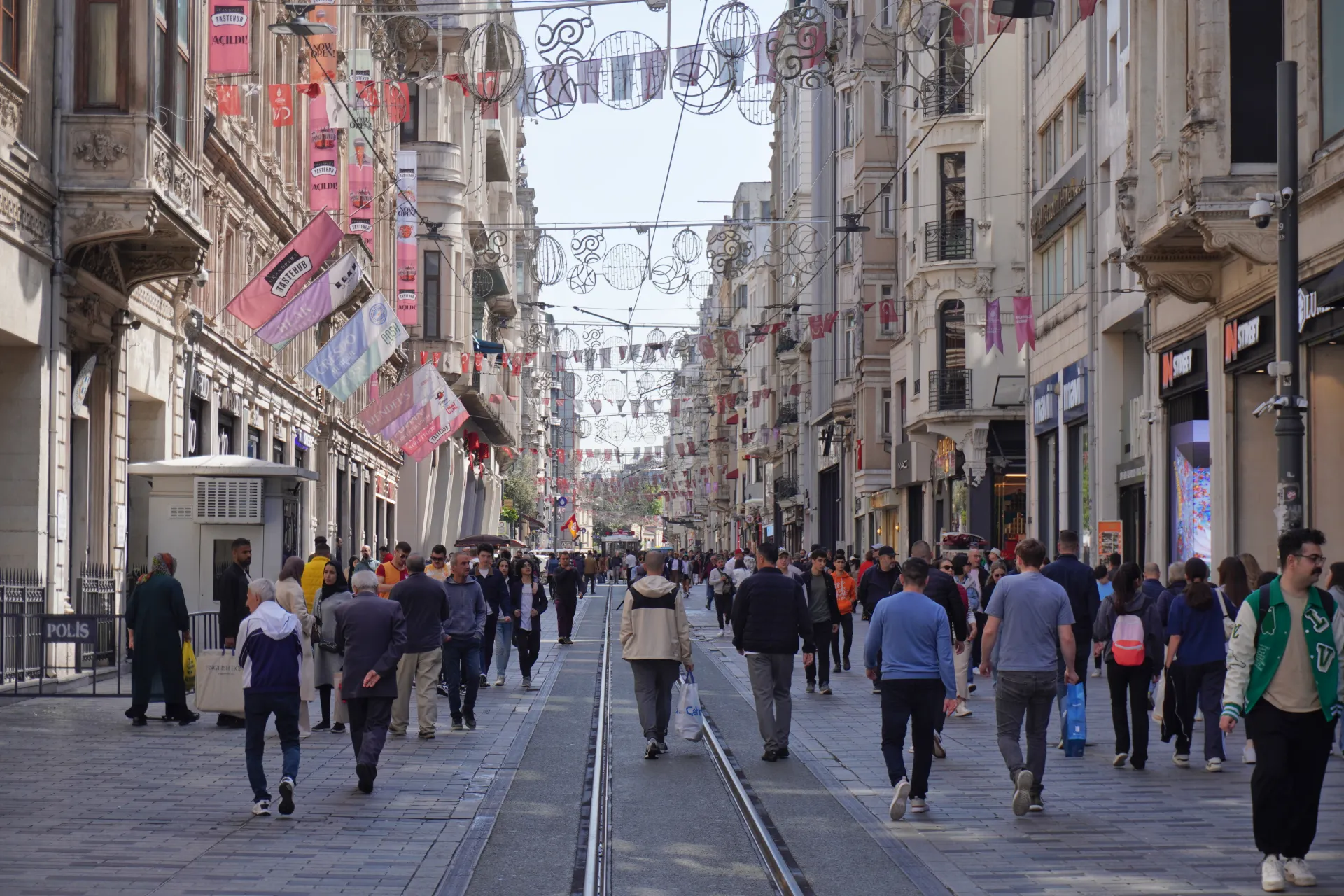 People walking on Istiklal Avenue in Istanbul, with shops and decorative banners lining the street.