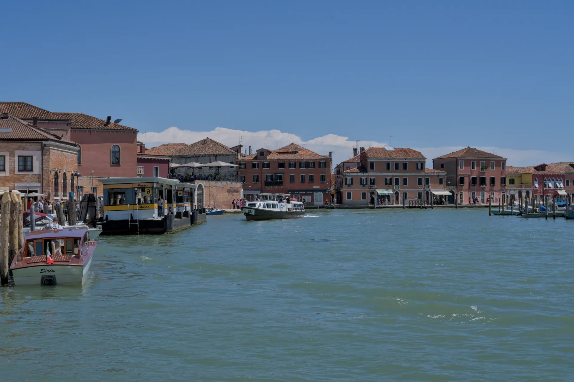 Kanal na ostrvu Murano, Italija, sa vodom, čamcima i kućama u pozadini.
