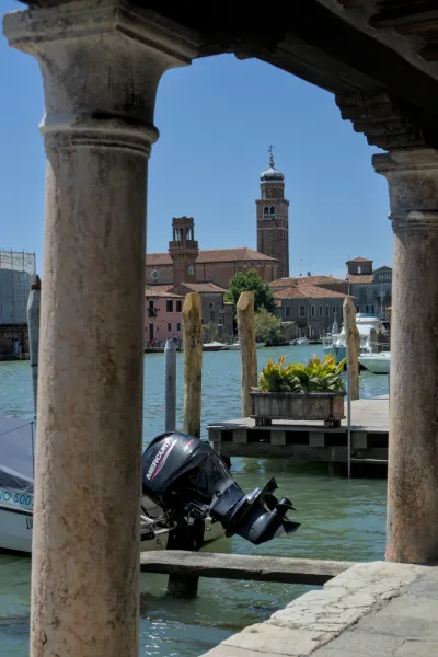 Blick durch antike Säulen auf die Insel Murano in Venedig mit türkisfarbenem Wasser und Kirchtürmen.
