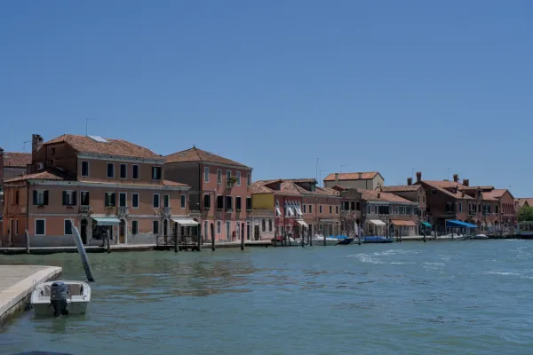Gebäuderei mit Terrakotta-Dächern am Wasser auf der Insel Murano, Italien, mit ruhigem blauem Wasser.