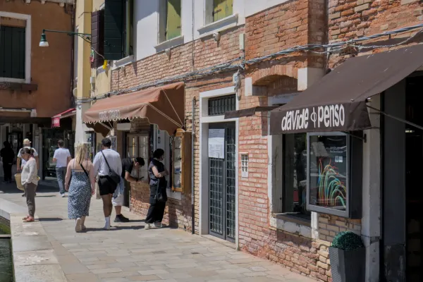 Fassade einer Kunstgalerie auf der Insel Murano mit Menschen, die davor spazieren, an einem sonnigen Tag.