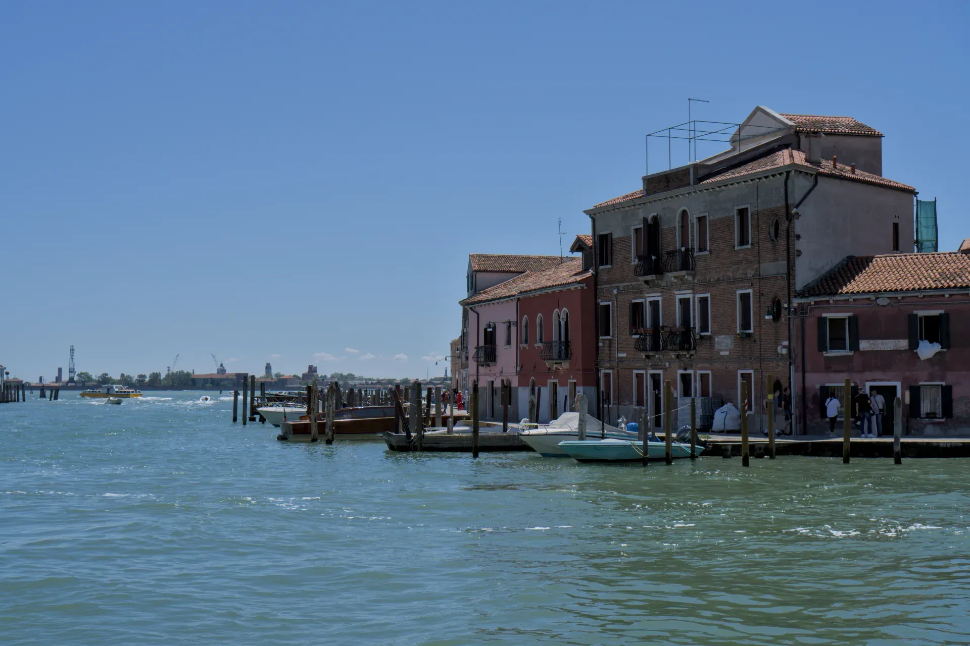 Colorful buildings on the canal bank of Murano, Italy, with boats at the quay.