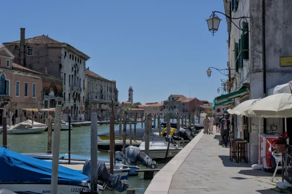 Ein Blick auf einen Kanal in Venedig mit Booten, die am Kai liegen, und traditionellen Häusern im Hintergrund, mit einer Ferne auf Murano