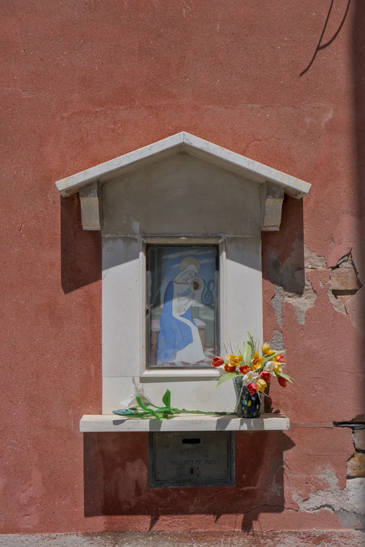 Madonna painting and flowers against a reddish wall on the island of Murano.