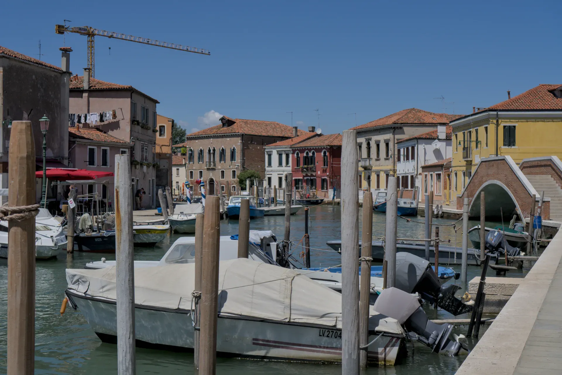 Boats in a canal on Murano island, Venice, with colorful houses and a blue sky.