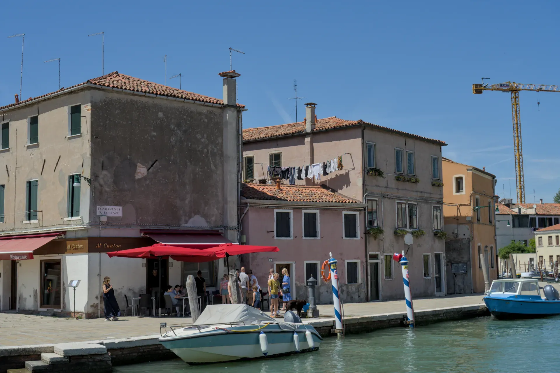 Photograph of the canal bank on Murano island, showing houses, laundry, and boats in the water.