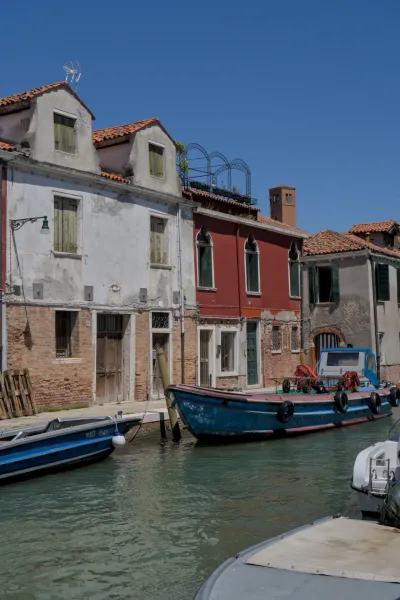 Mirna ulica na ostrvu Murano u Veneciji sa tradicionalnim zgradama i čamcima u vodi.