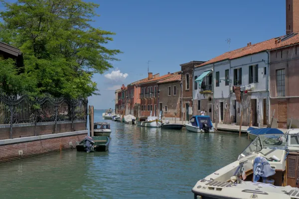 Kanal na Muranu, Italija, obrubljen šarenim kućama i čamcima, pod vedrim plavim nebom.
