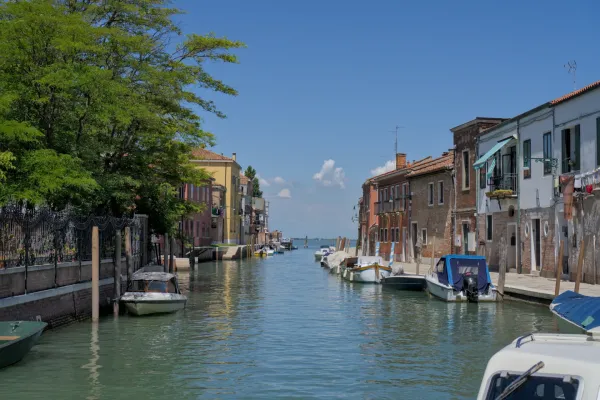 Mirni kanal na ostrvu Murano u Veneciji, poredan šarenim kućama i čamcima u tirkiznoj vodi.