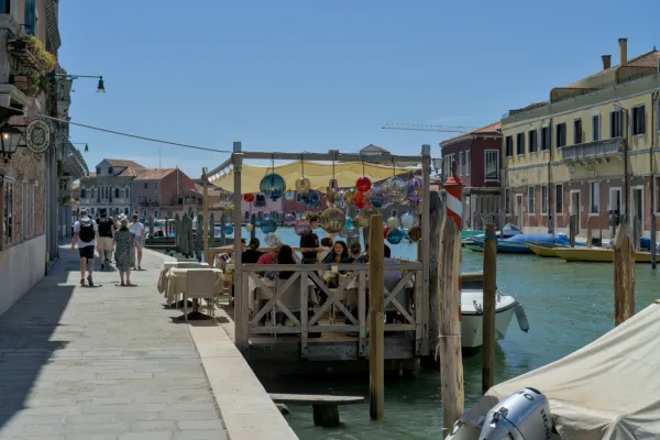 Kanal u Murano sa restoranom i šarenim staklenim svetiljkama, u pozadini tradicionalne zgrade i čamci.