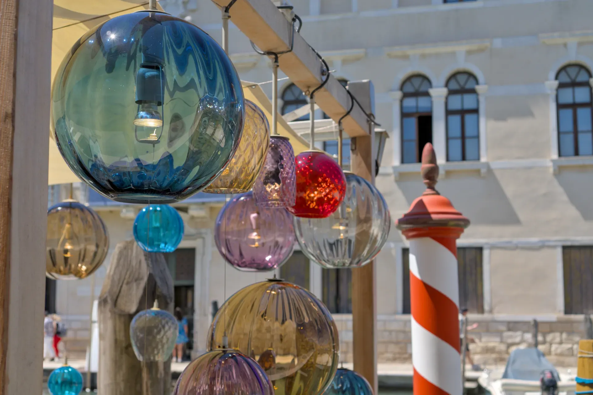 Lampes en verre de Murano colorées suspendues au-dessus d'un canal en Italie, avec la façade d'un bâtiment en arrière-plan, inspirées d'un café.