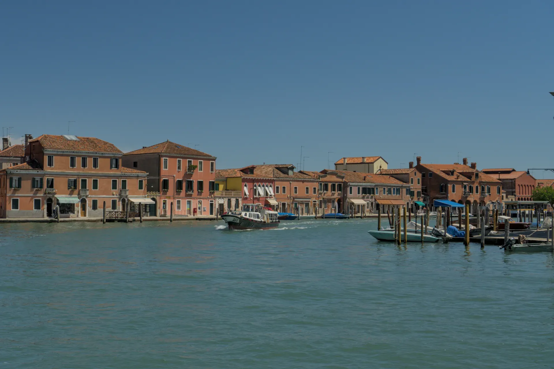 Blick auf den Kanal von Murano mit bunten Häusern und einem vorbeifahrenden Boot.