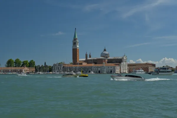 Crkva San Giorgio Maggiore u Veneciji, Italija, sa čamcima na Kanalu Grande pod plavim nebom.