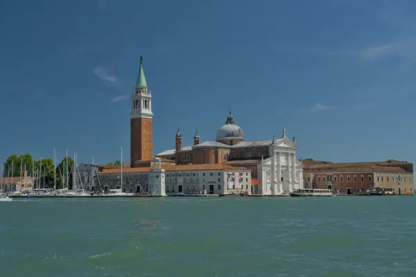 Bazilika San Giorgio Maggiore sa kampanilom u Veneciji, Italija, na pozadini vedrog plavog neba i mirne vode.