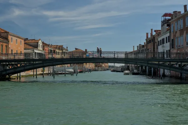 Detaljna fotografija mosta u Veneciji, Italija, preko tirkiznog kanala, sa tradicionalnim zgradama i parom koji šeta.