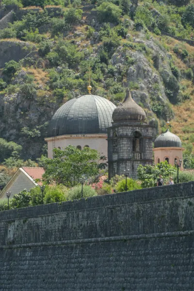 Vista in formato ritratto degli antichi muri della città e delle cupole delle chiese di Kotor, Montenegro, sullo sfondo di una lussureggiante montagna.