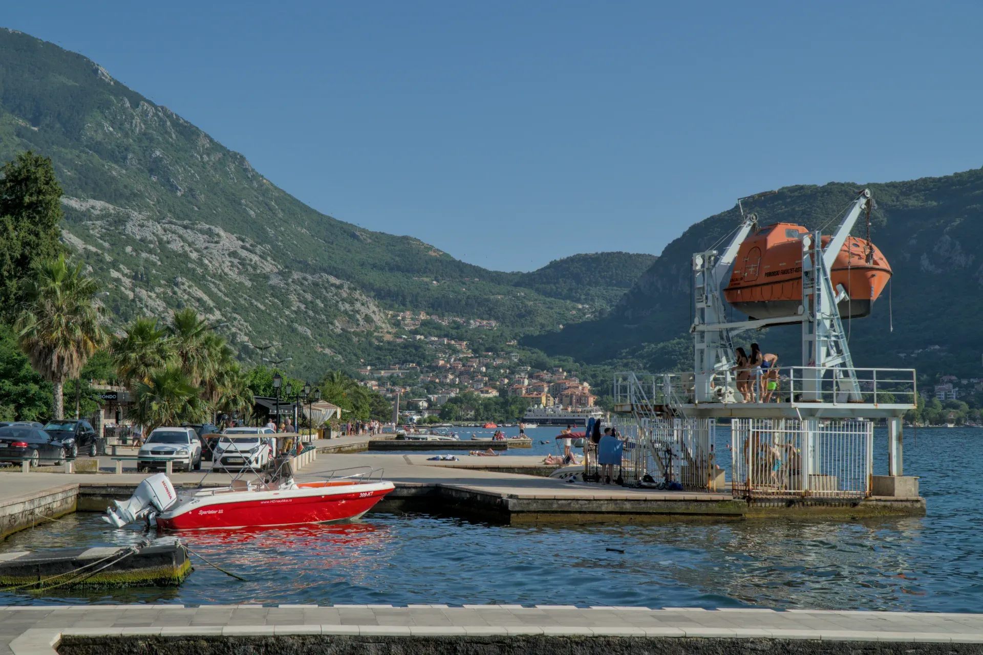 A picturesque view of the Bay of Kotor in Montenegro with a red boat and life rafts on a sunny day.