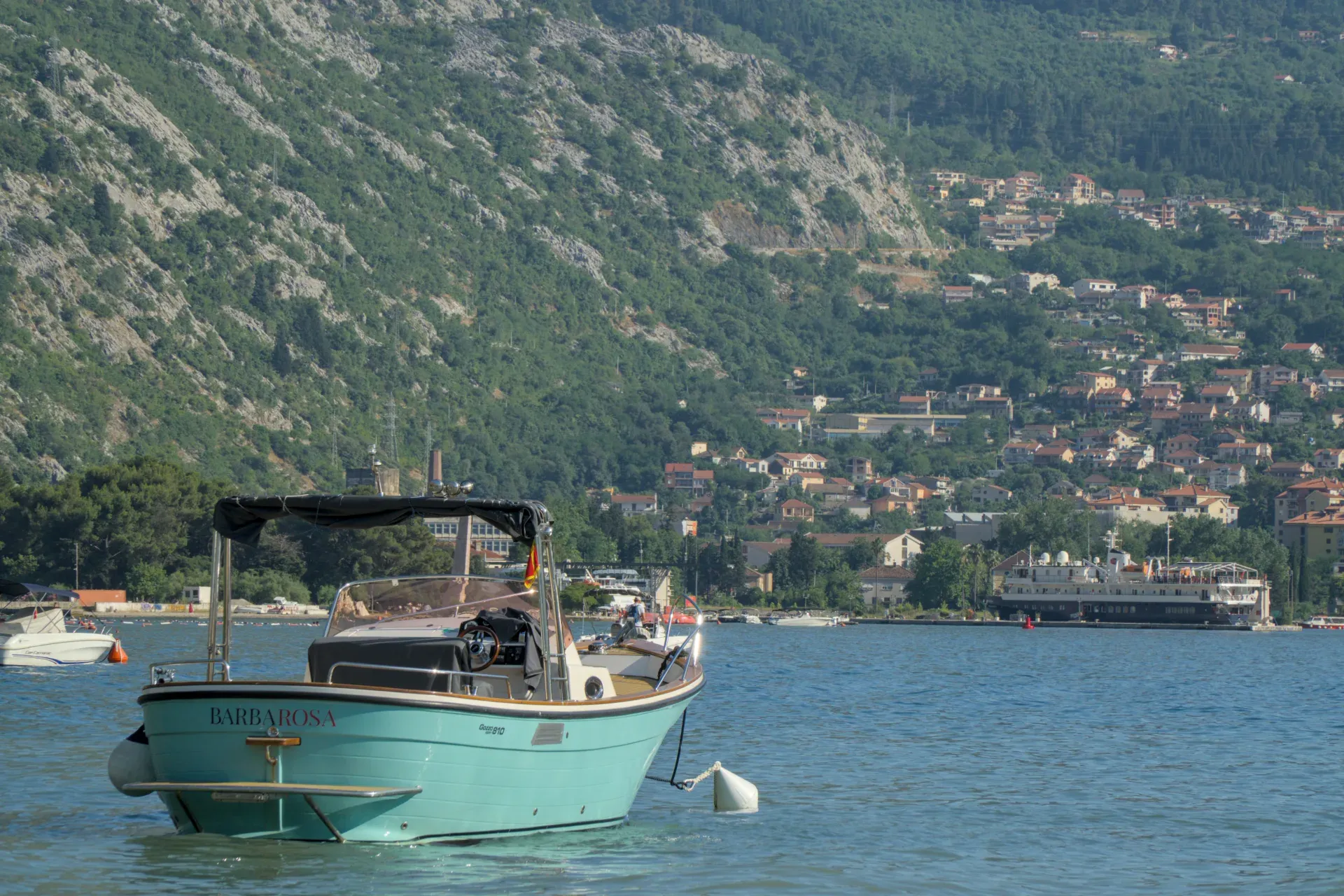 A turquoise boat rests off the coast of the Bay of Kotor, Montenegro, with green hills in the background.