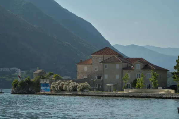 Edificio histórico en la Bahía de Kotor con montañas al fondo y una estructura similar a un faro.