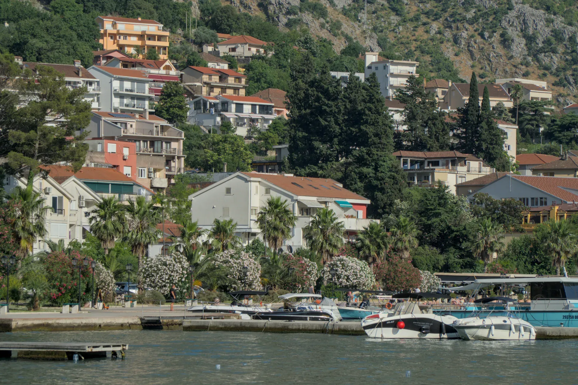 Landscape photography of the coast of Kotor, Montenegro, with houses on a hill and boats in the water.
