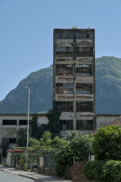 Un edificio decrépito de varios pisos en Kotor, Montenegro, con ventanas y un paisaje montañoso al fondo.