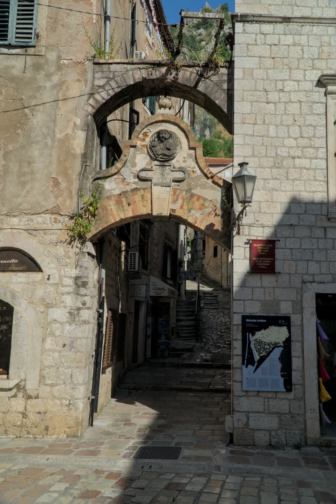 Stari kameni lučni prolaz u Kotoru, Crna Gora, sa senkama i svetlom na kaldrmi i zgradama.
