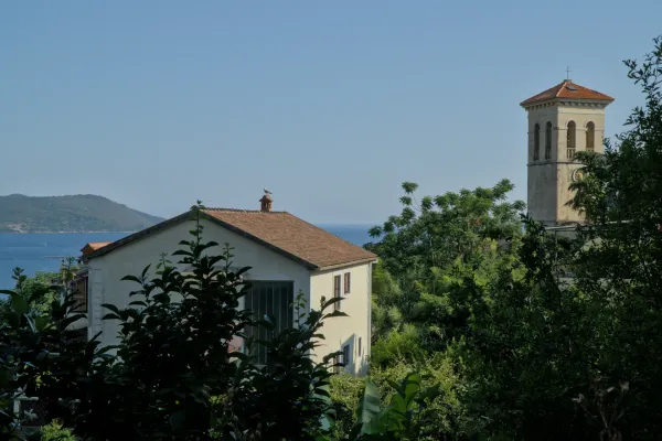 Una casa mediterránea tradicional con tejado de tejas y vistas al mar, junto a un destacado campanario en Herceg Novi, Montenegro.