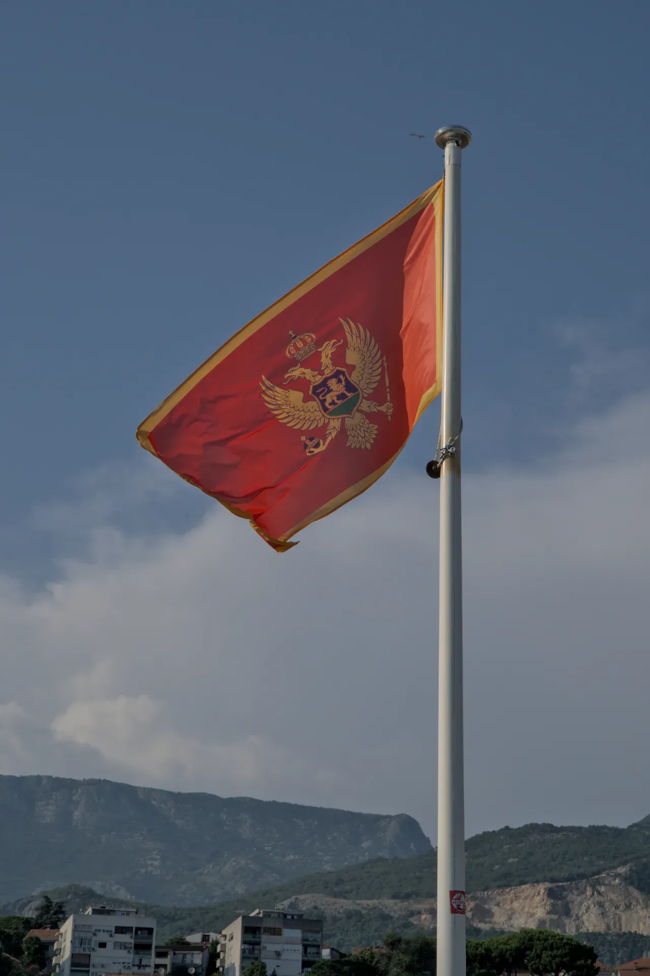 Montenegrin flag with coat of arms waving in the wind against a blue sky over Herceg Novi