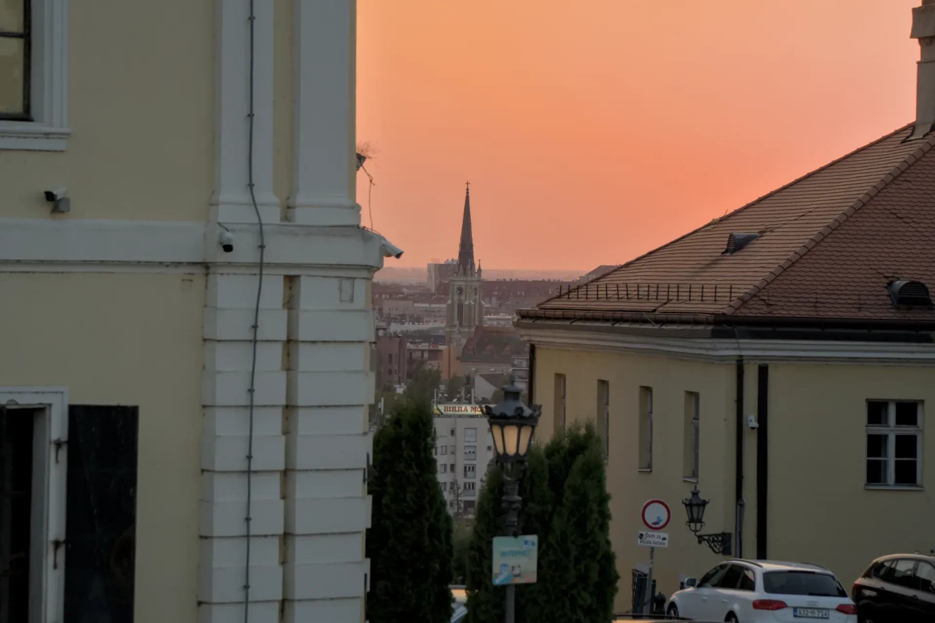 View of the Sacred Heart Church with its distinctive spire, seen from Petrovaradin Fortress, during an orange sunset.