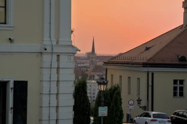 View of the Sacred Heart Church with its distinctive spire, seen from Petrovaradin Fortress, during an orange sunset.