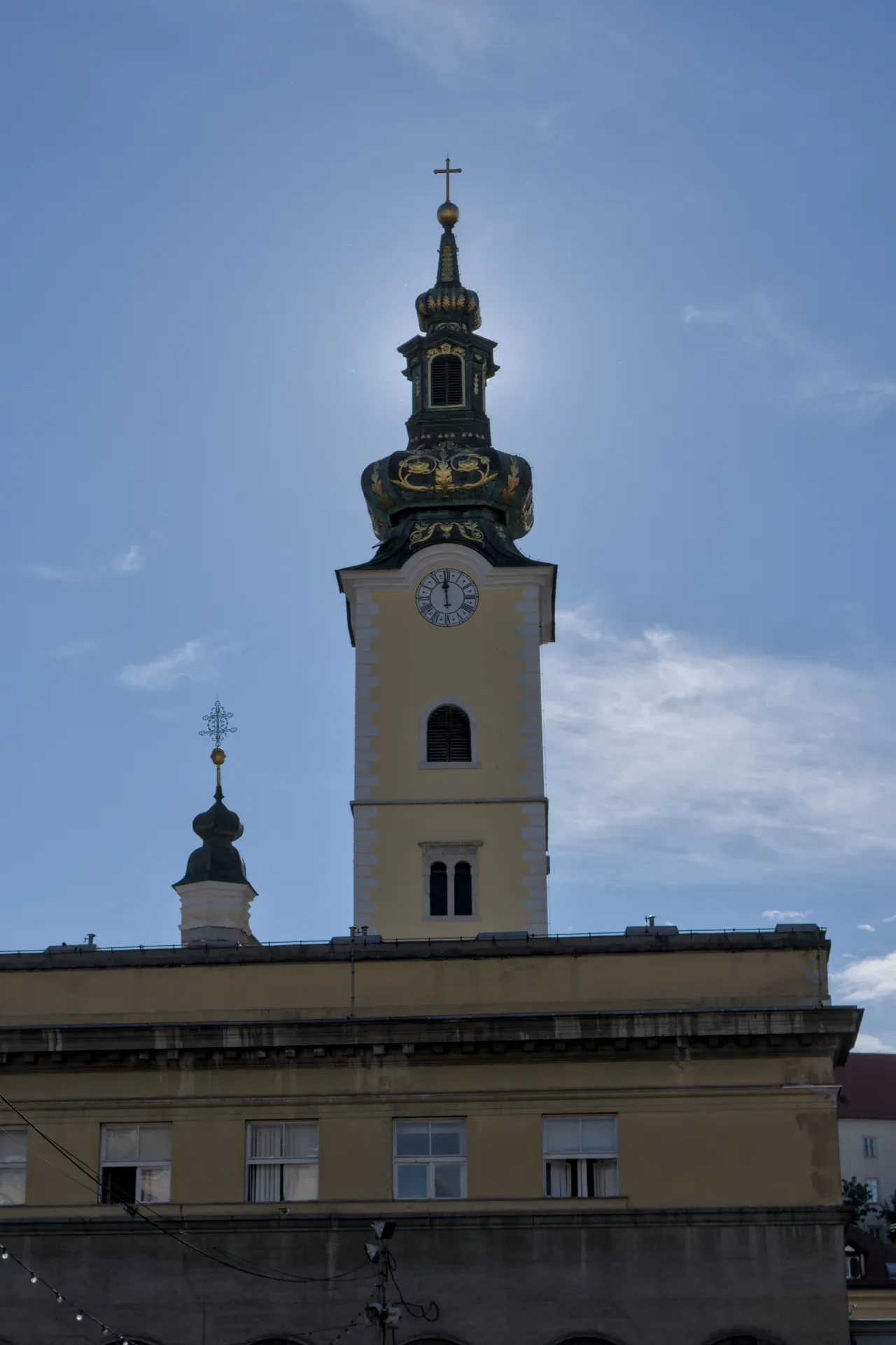 A vertical photo of a historic tower with a golden dome and clock in Zagreb, Croatia, against a blue sky.