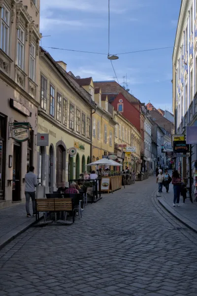 A bustling street in Zagreb with café tables and traditional architecture under a blue sky.