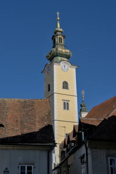 Un clocher détaillé avec une horloge et des ornements dorés ouvragés, sur un ciel bleu éclatant, capturé à Zagreb.