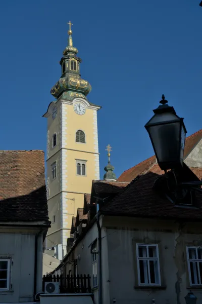Una foto di ritratto di un campanile giallo con cupola verde e decorazioni dorate, catturato contro il cielo azzurro limpido sopra Zagabria.