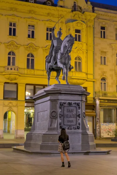 Monument de Ban Jelačić la nuit avec une statue équestre et une personne qui le regarde.