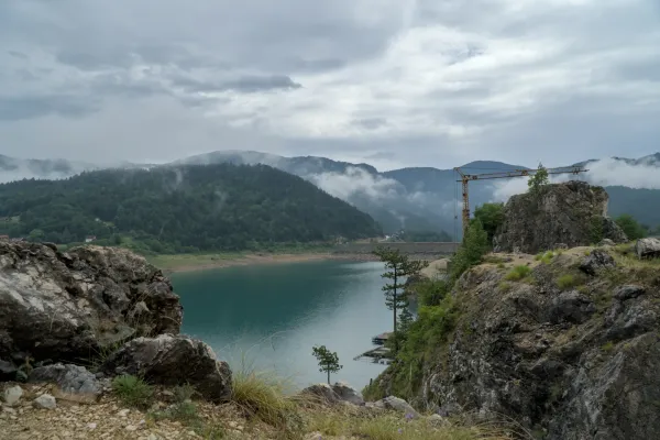 Paisaje agreste en el lago Zaovine con niebla y nubes, enmarcado por rocas, árboles y montañas.