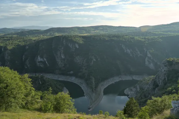 Der Uvac Canyon in Serbien mit seiner markanten Flussbiegung bei Sonnenuntergang, umgeben von bewaldeten Hügeln.